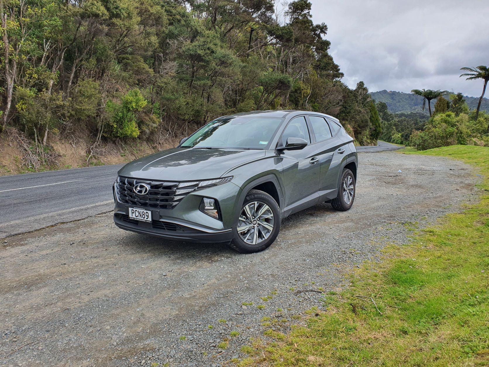 Front three quarters view of a 2022 Hyundai Tucson Hybrid in green with a nature backdrop