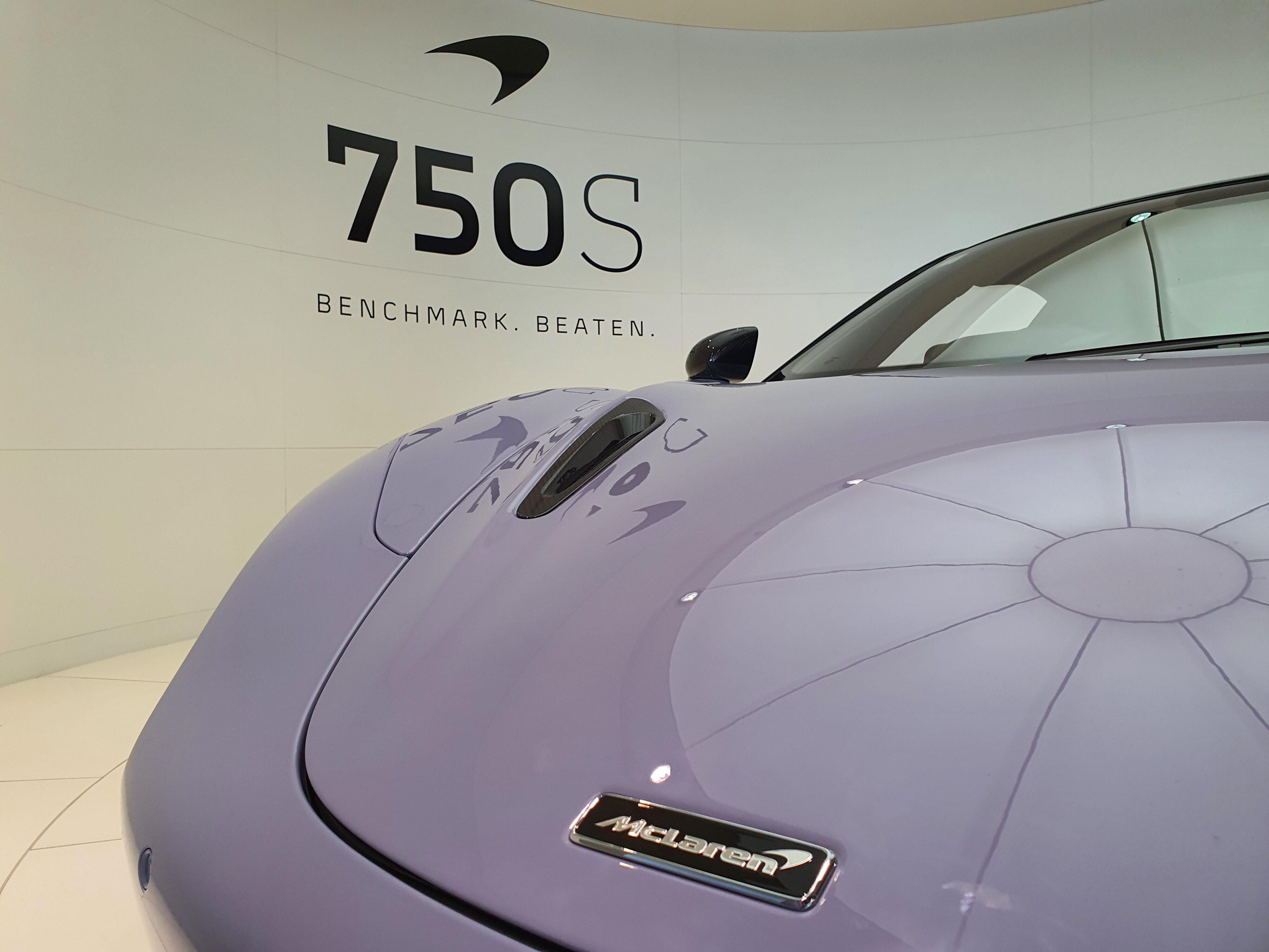 Close up of the McLaren badge on the front of a new 750S with the car's name in the background.