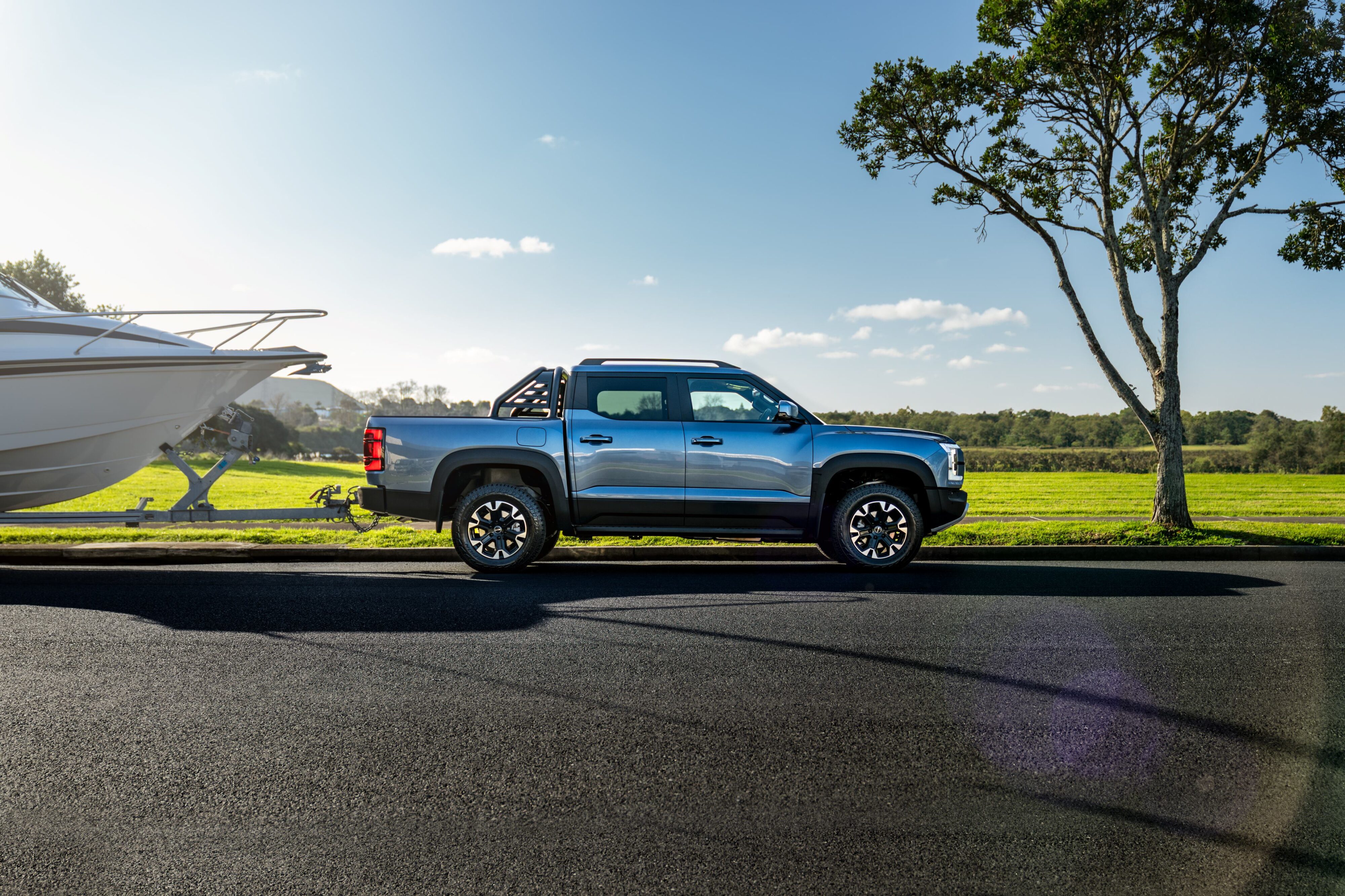 Side view of a BYD Shark 6 towing a boat with the ocean in the background.