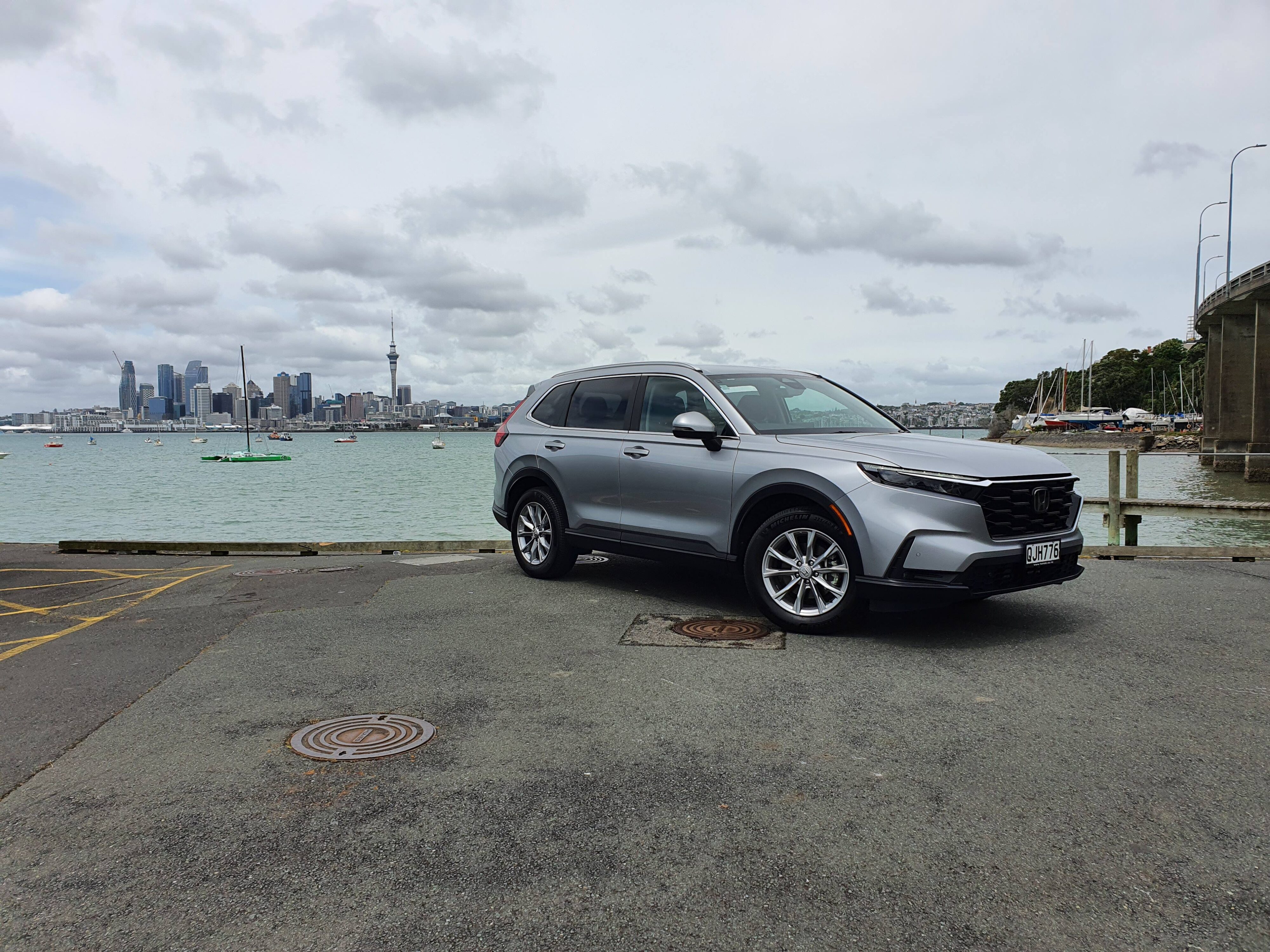Front three quarters view of a 2024 Honda CR-V AWD in Silver with Auckland's city skyline in the background.