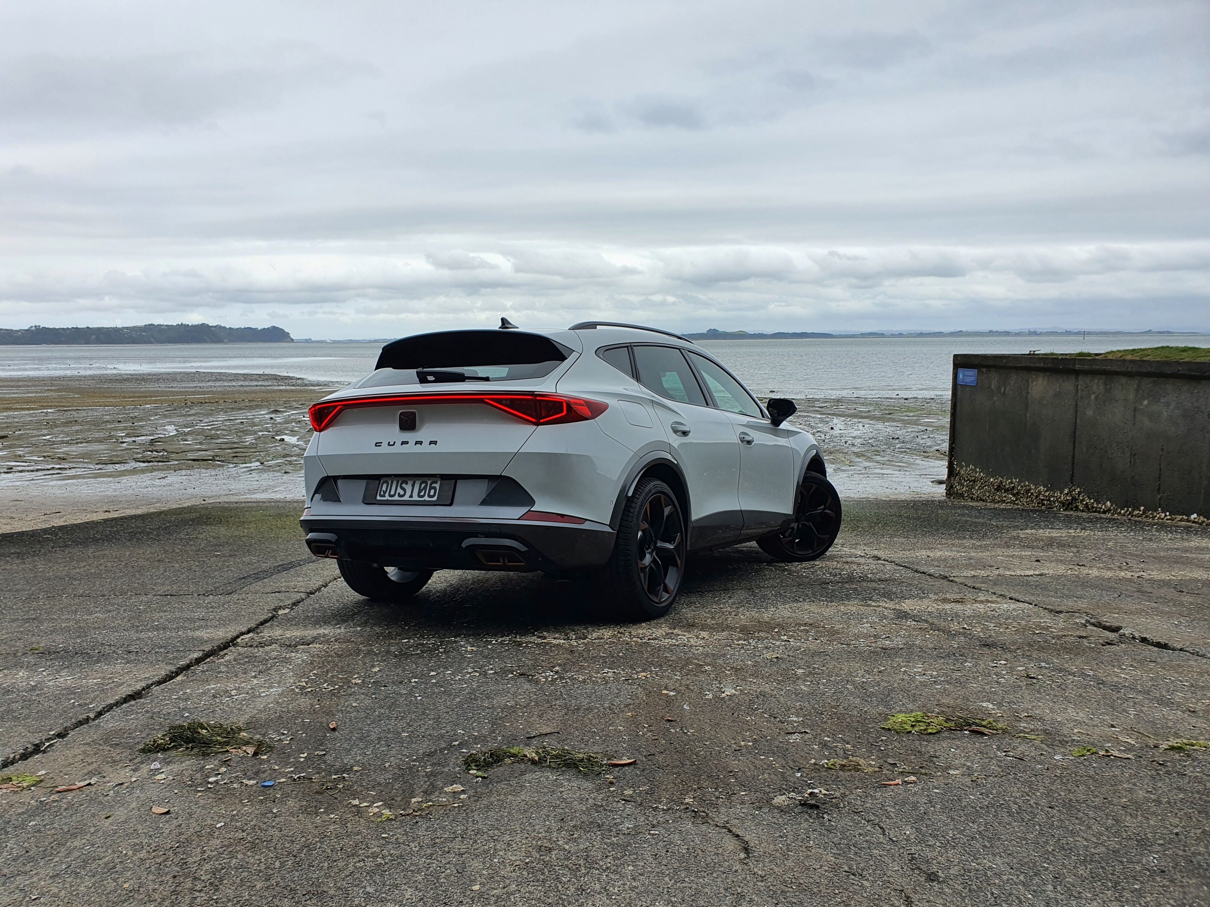 Rear three quarters view of a 2024 Cupra Formentor V e-Hybrid in white on a boat ramp. 