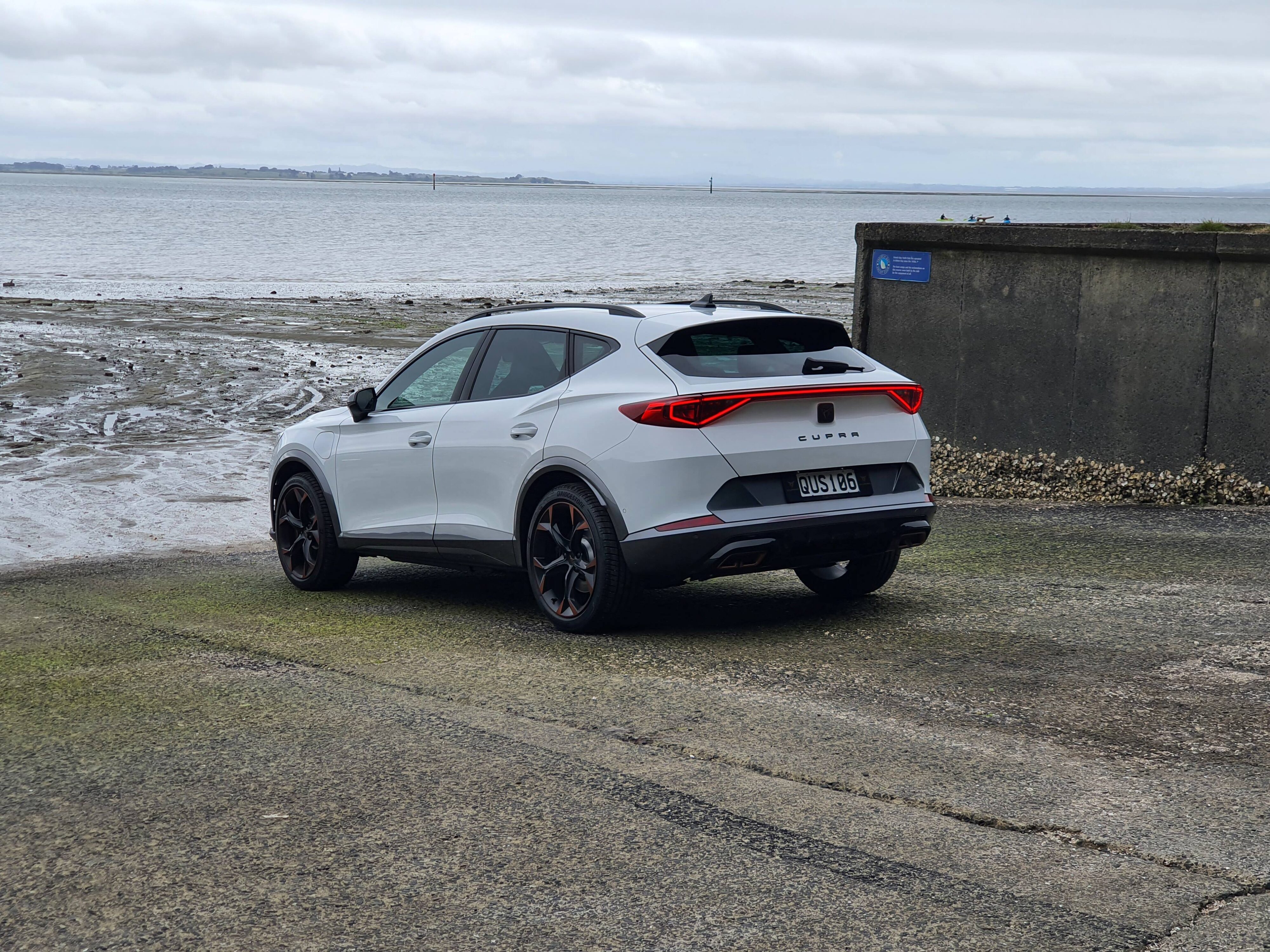 Rear three quarters view of a 2024 Cupra Formentor V e-Hybrid in white on a boat ramp. 