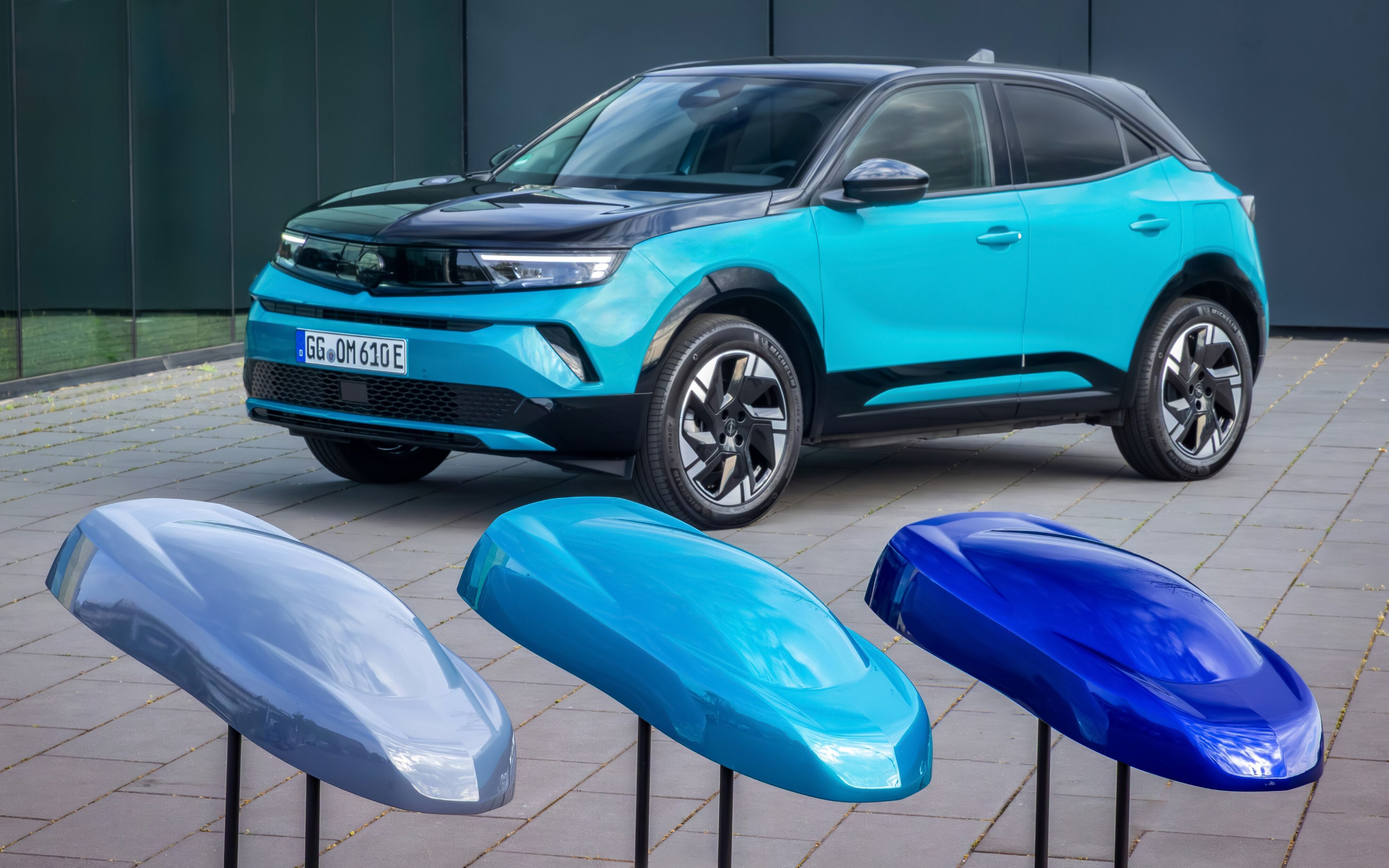 An Opel Mokka e in Tropikal Green in the background with the three new colour options in the foreground.
