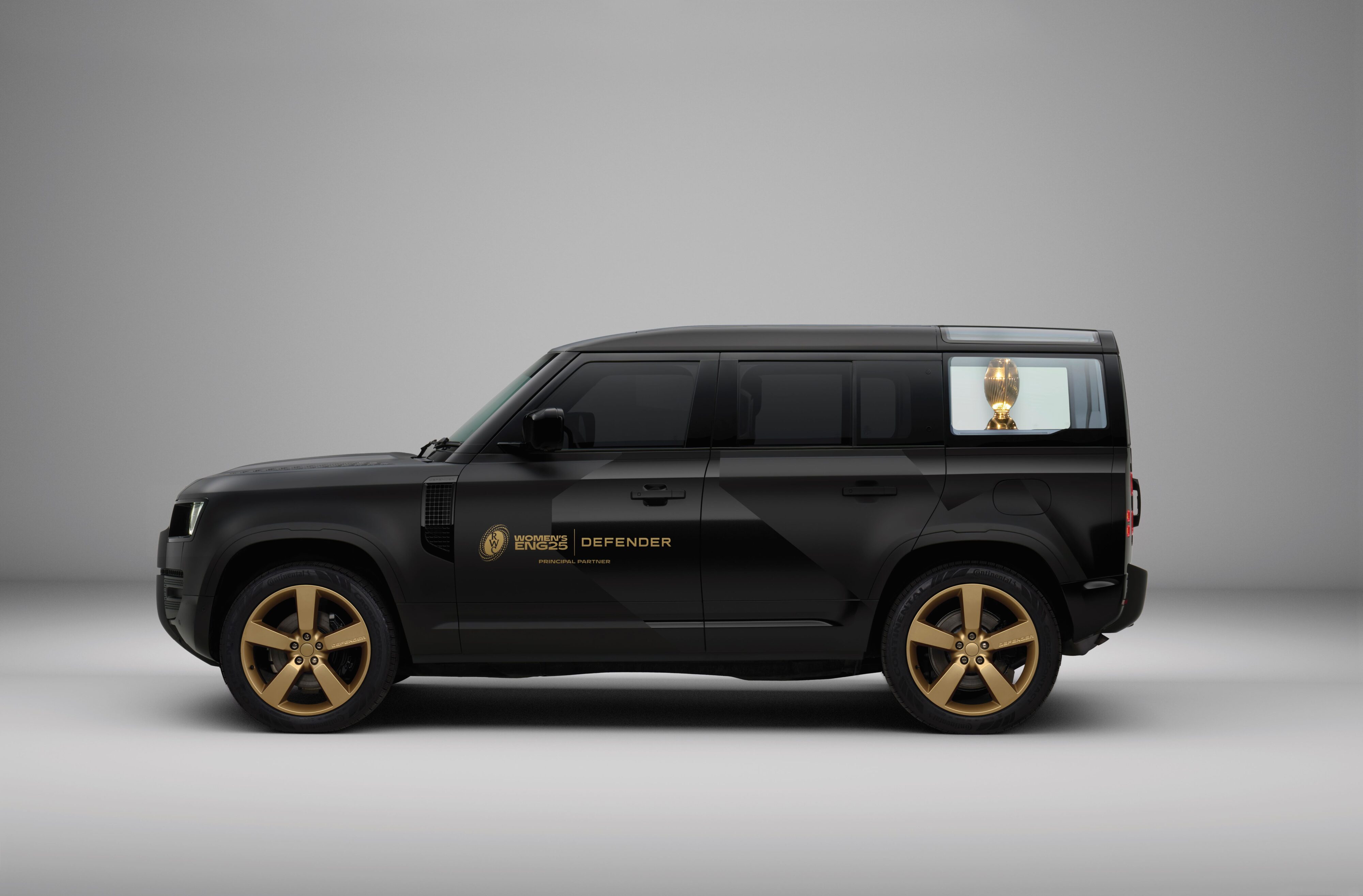 Side on view of a custom Defender 110 with the Women's Rugby World Cup 2025 trophy in the back.