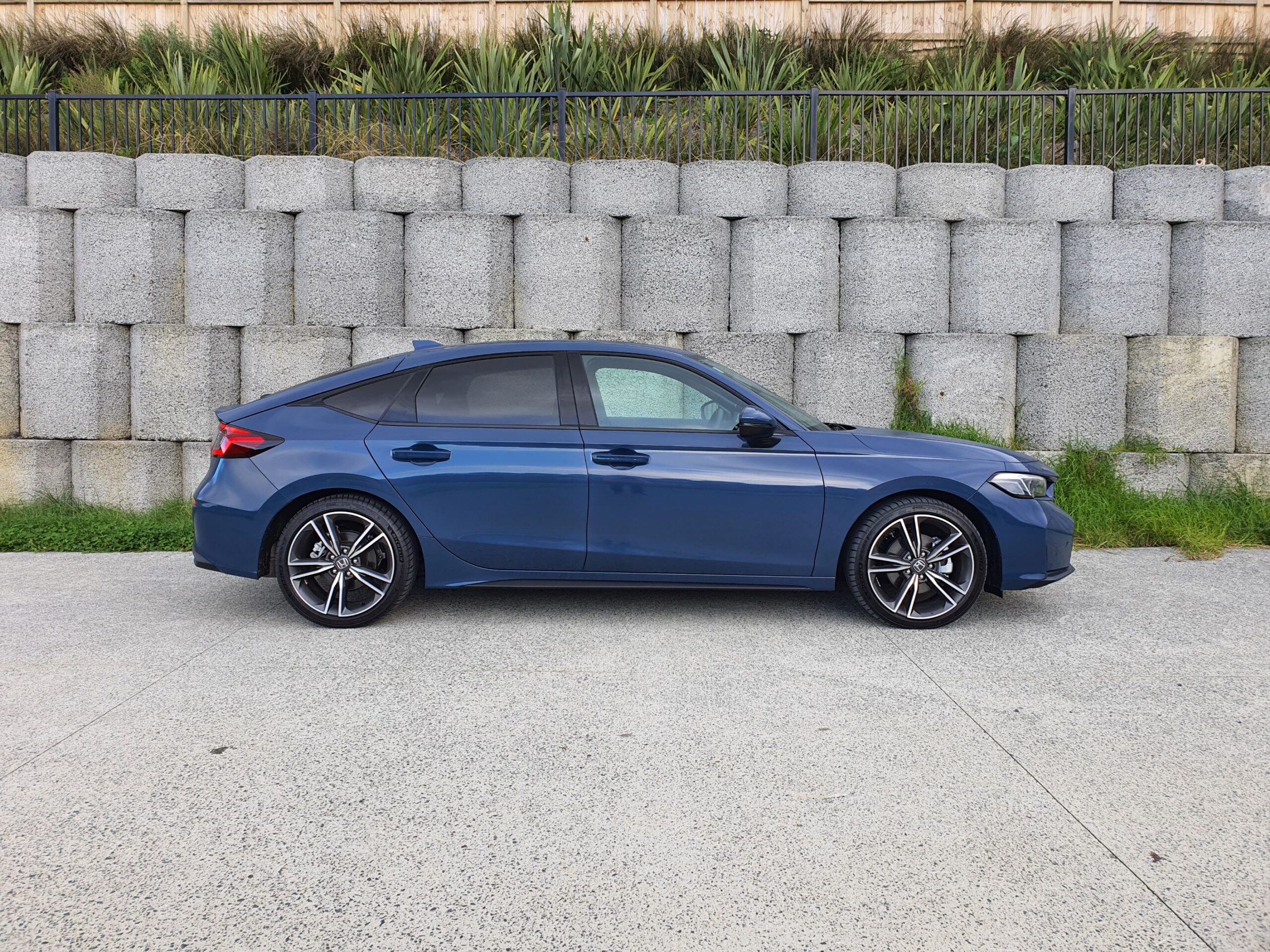 Side on view of a 2025 Honda Civic e:HEV in Ocean Blue Pearl in an urban setting.