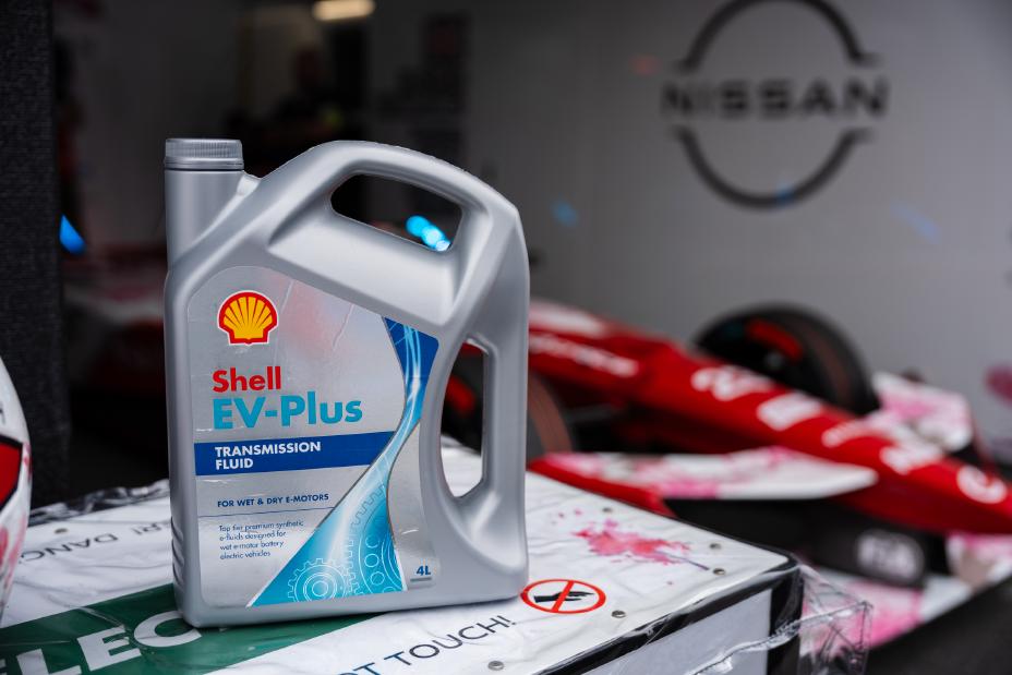 A photo of a Shell EV Plus transmission fluid bottle in from of a Nissan Formula E racecar.