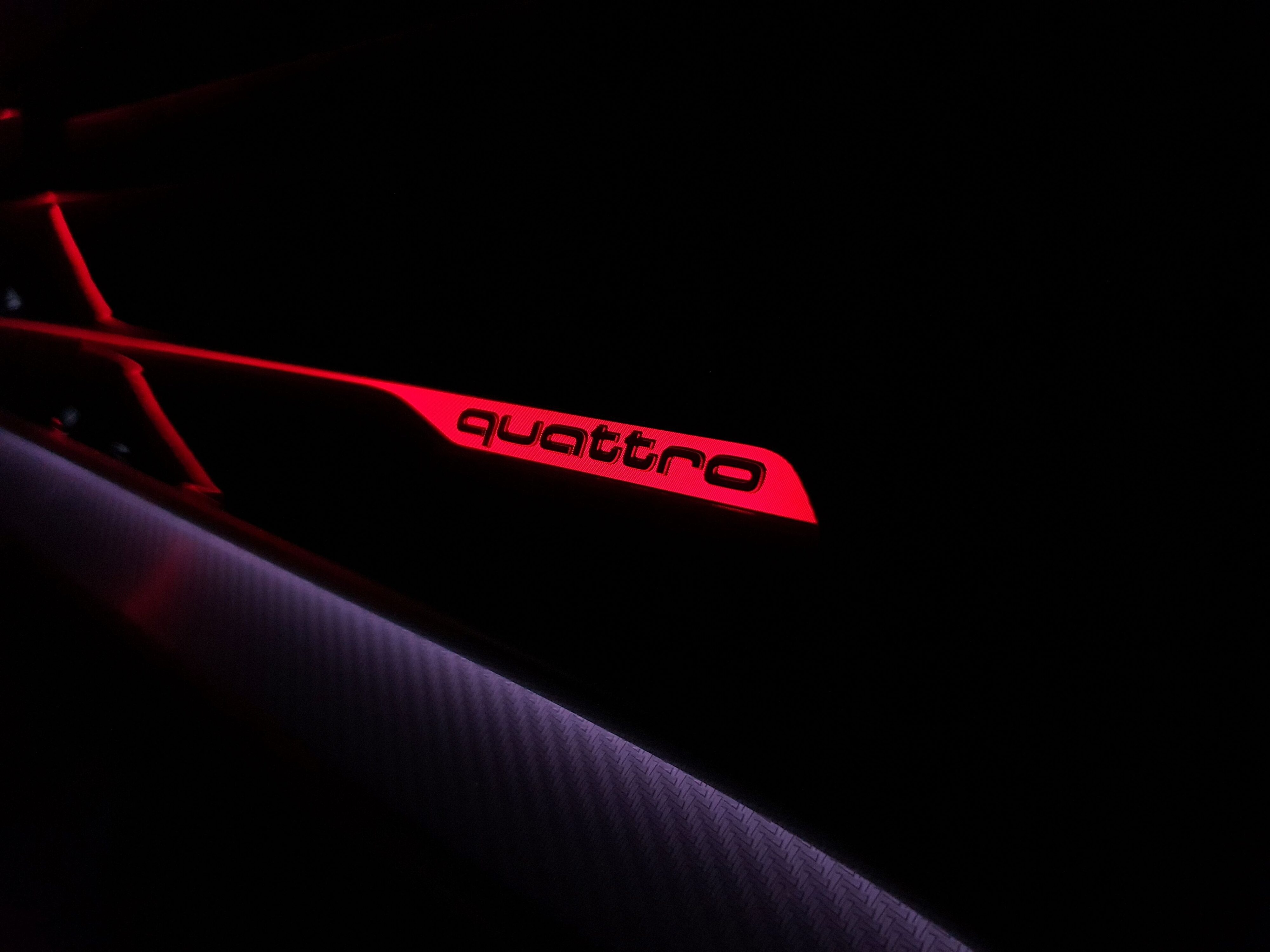 Red illuminated Audi 'quattro' badging on the interior dashboard panel of a 2025 Audi RS Q8 Performance.