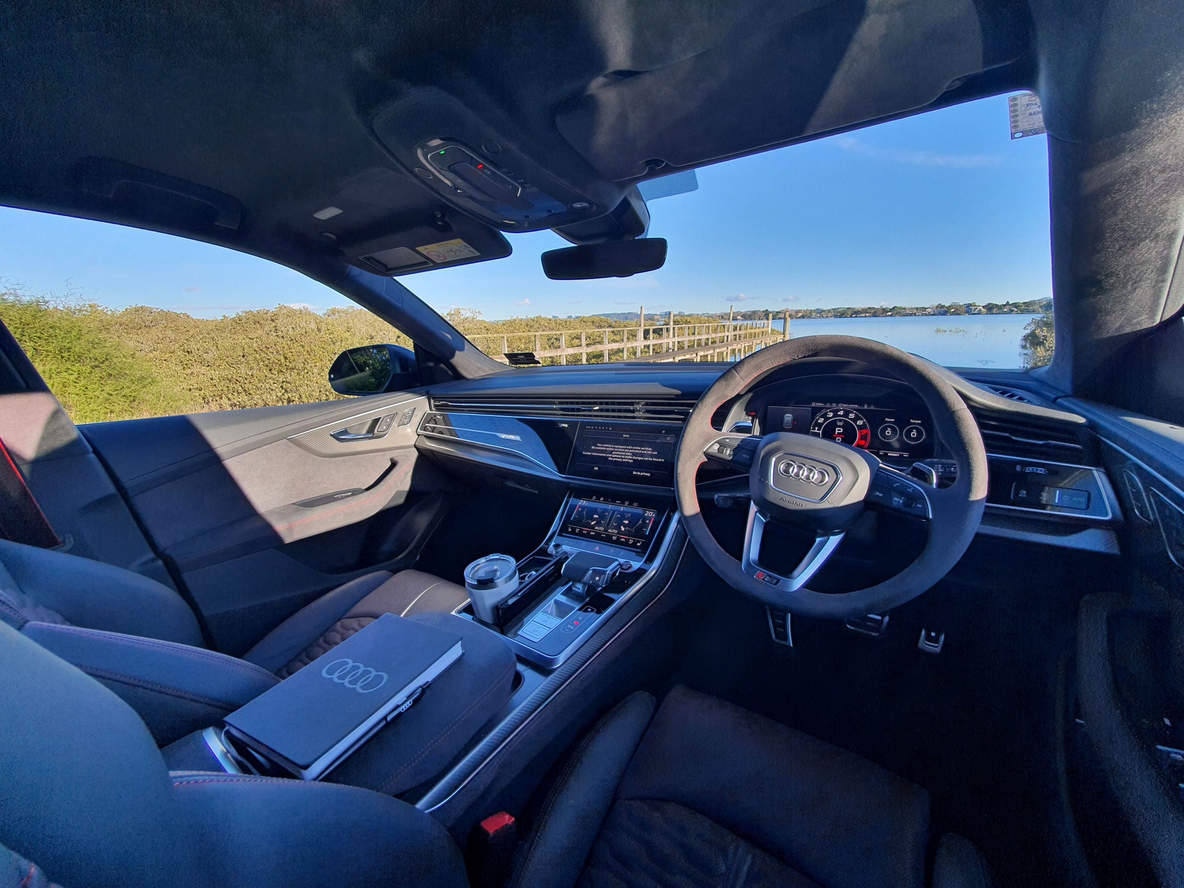 Interior view of a 202 Audi RS Q8 Performance in Chili Red. View out the windscreen is of a lagoon/water body inlet.