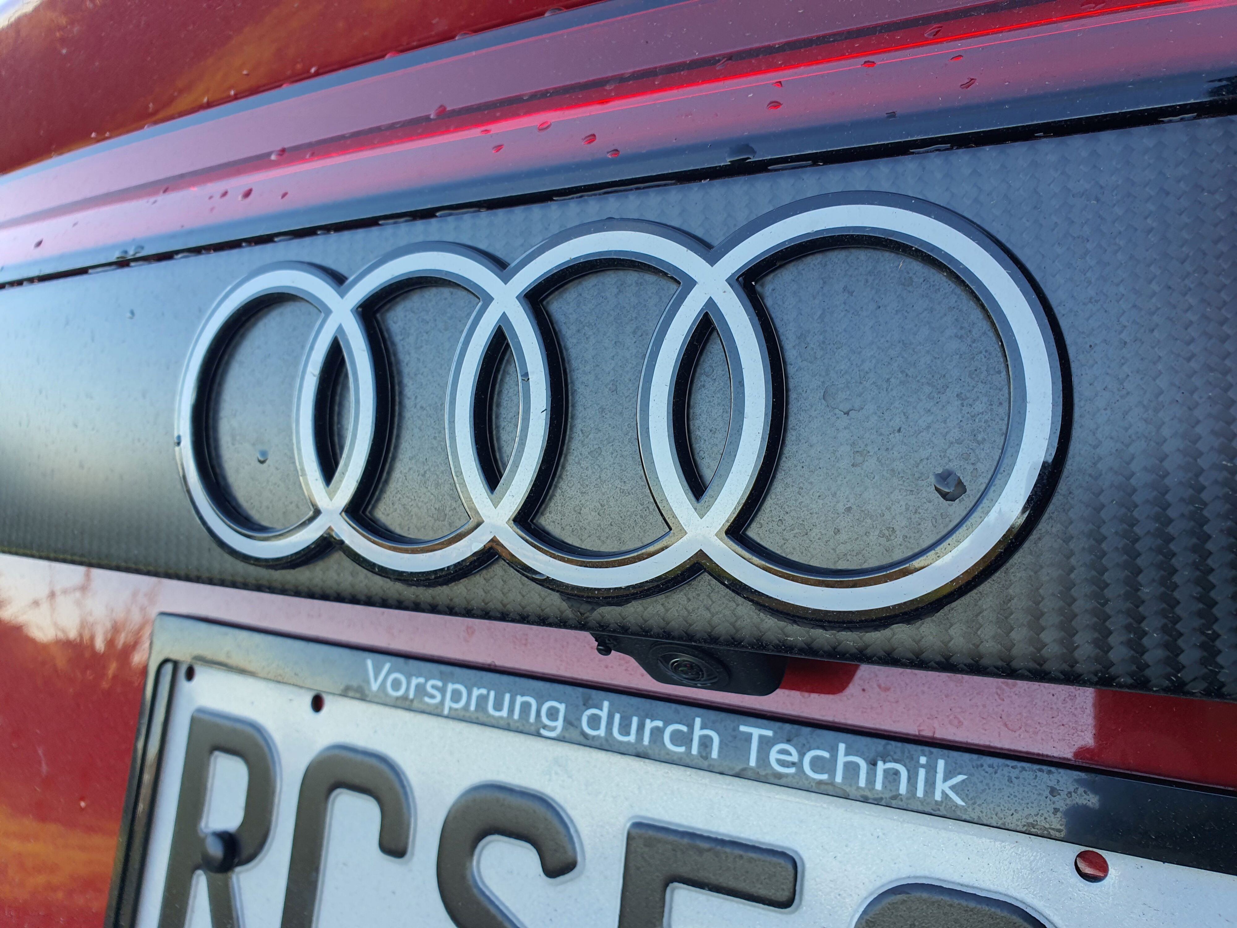 The four interlocked rings of the Audi badge as seen on the rear carbon panel of a 2025 RS Q8 Performance in Chili Red.