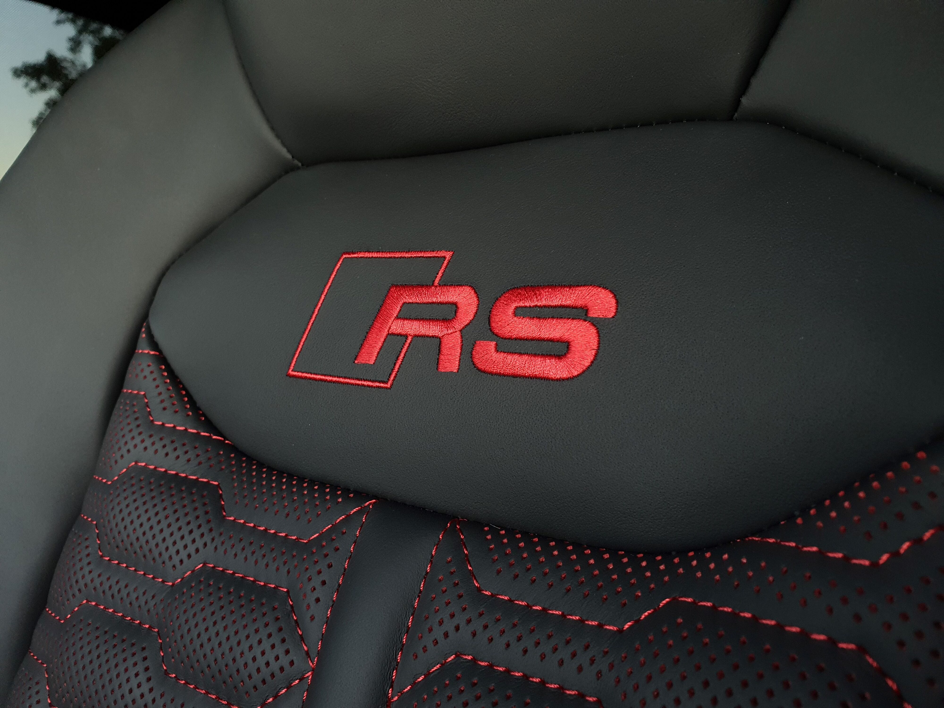 Red stitched Audi Sport RS badging on the black leather seatback of a 2025 RS Q8 Performance.